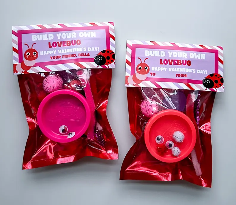 Two red foil bags containing a "Build Your Own Lovebug" kit, featuring Play-Doh, googly eyes, and pom-poms, perfect for Valentine's Day Party Favors.