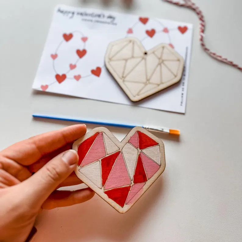 A wooden geometric heart shape, paintbrush, and paint, shown being decorated, as a unique DIY Valentine's Day Party Favors kit. Etsy