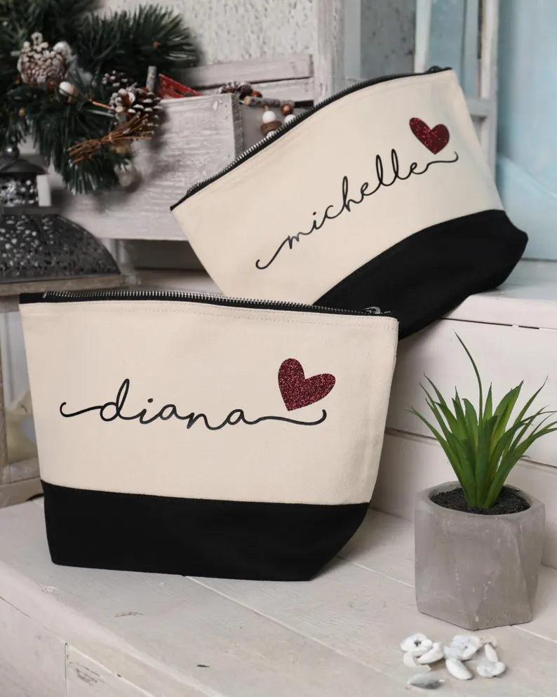 Two personalized canvas makeup bags with glitter hearts and names like "Michelle" and "Diana," stylish Galentine's Day Party Favors.