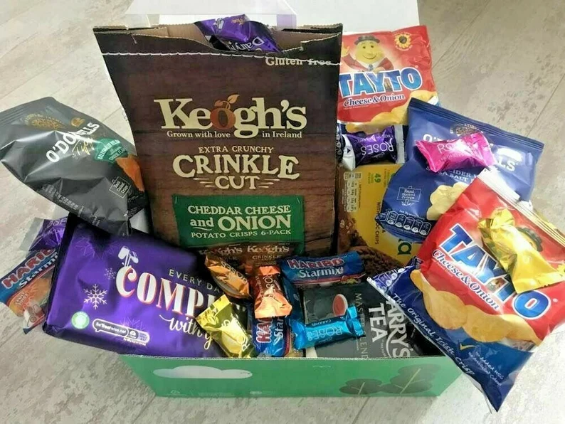 A green gift box overflowing with iconic Irish snacks like Tayto crisps and Keogh's, serving as festive St. Patrick's Day favors.