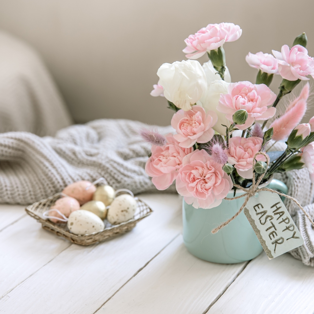 eggs in a small basket with a vase of pastel pink and white flowers and a tag saying happy easter