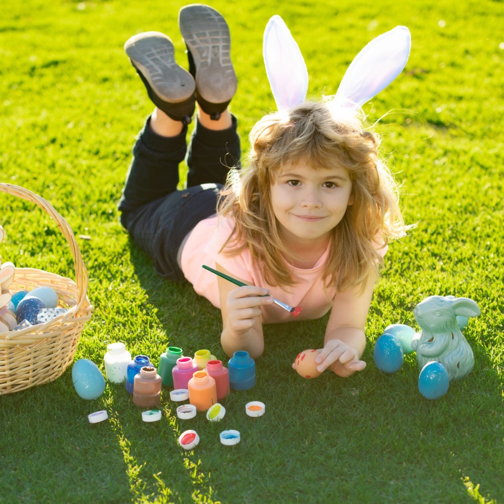 a cute child with bunny ears playing with eggs in the grass