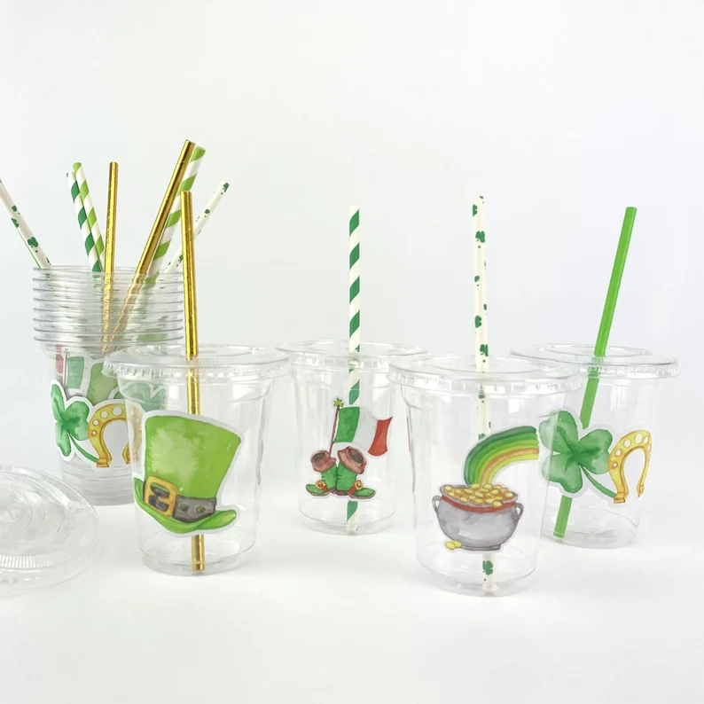 Clear plastic party cups decorated with shamrocks and gold coins, featuring festive straws as coordinated St. Patrick's Day favors.