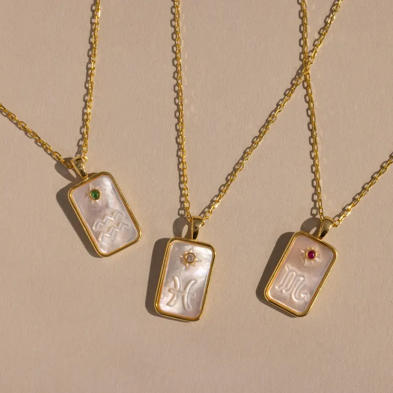 Mother of pearl zodiac pendants with inlaid birthstones on gold chains. Celestial astrology jewelry ideal for luxury birth month gifts and birthdays.