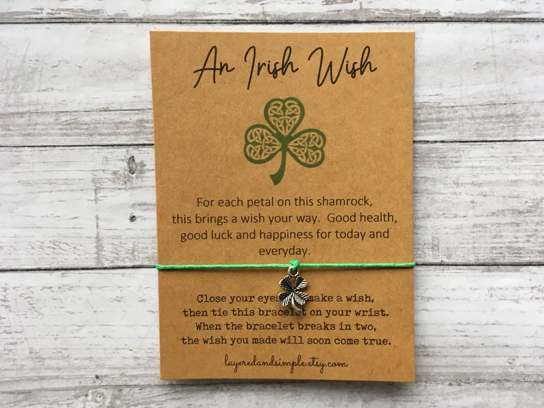 A green string "Irish Wish" bracelet with a silver shamrock charm, presented on a kraft card for meaningful St. Patrick's Day favors.