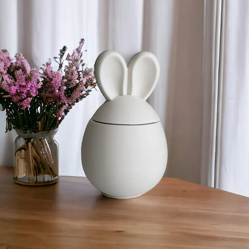 Minimalist white ceramic bunny-shaped jar with ears on a wooden table, a modern and stylish Easter hostess gift.