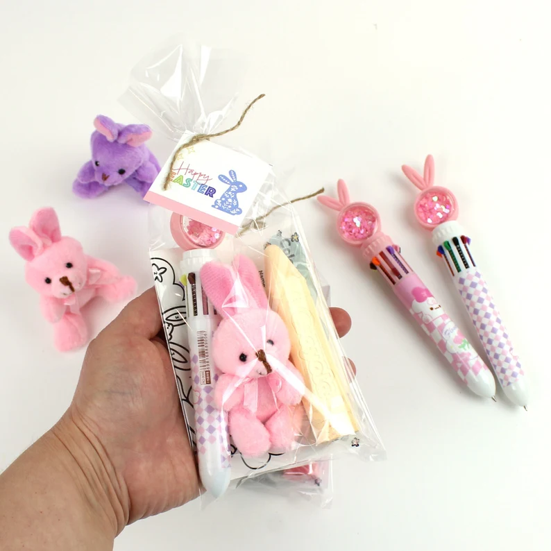 A clear gift bag containing a small plush bunny, multi-color pen, and crayons for creative Easter Party Favors Kids.