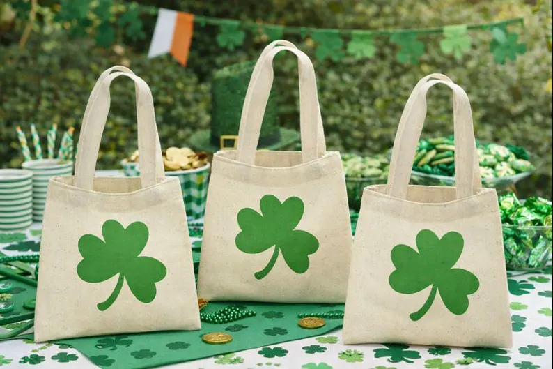Three canvas gift bags featuring large green shamrocks, perfect as reusable St. Patrick's Day favors for party treats.