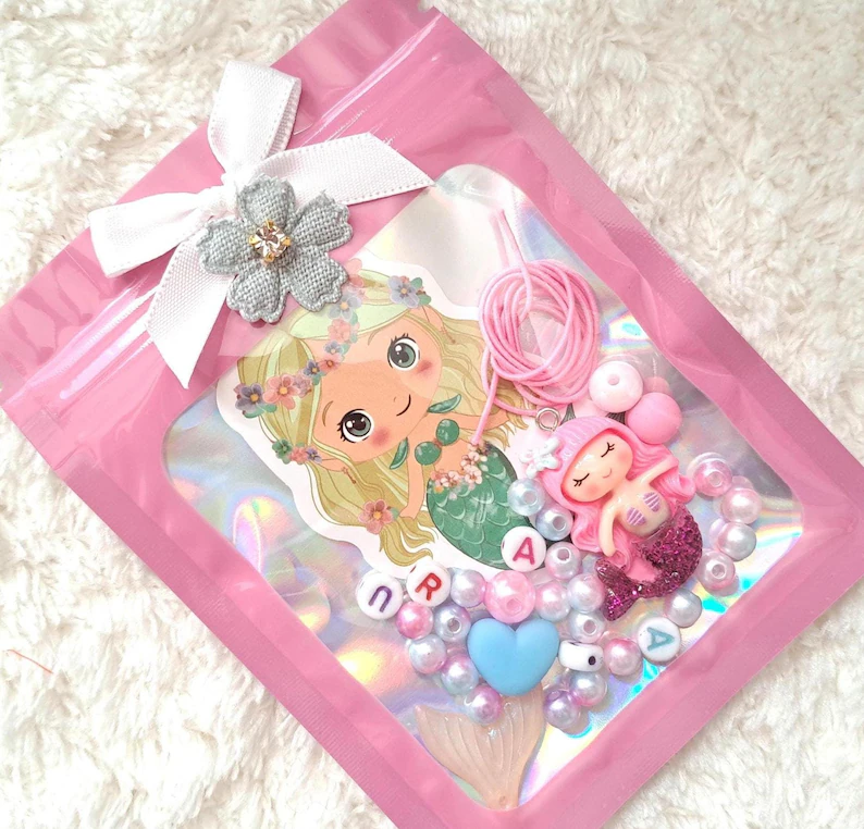 DIY bracelet kit with colorful beads, mermaid charm, and personalized letters packaged in pink holographic bag, ideal mermaid party favors for craft activities.