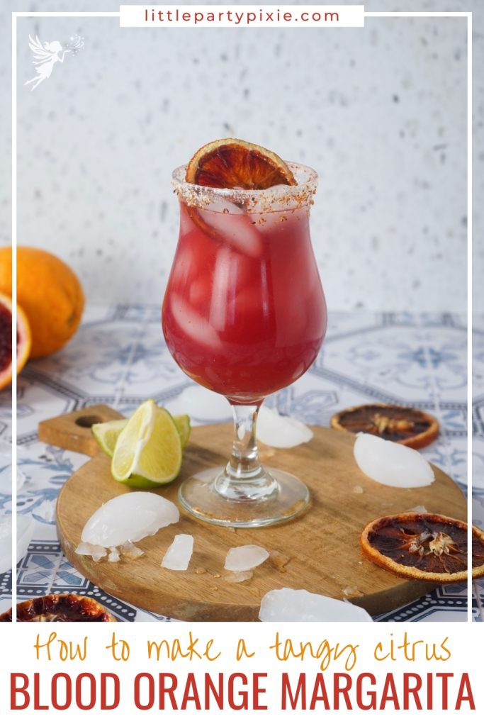 A refreshing Blood Orange Margarita served on a wooden board with lime wedges and scattered ice against a patterned tile background.