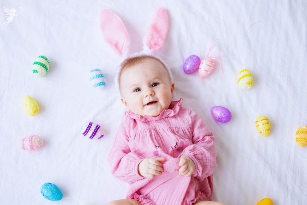 cute baby girl with easter ears lying on a white bed surrounded by easter eggs