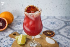 A vibrant Blood Orange Margarita filled with ice, featuring a chili-salted rim and a dried citrus wheel garnish.