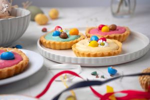 Gourmet Easter Cheesecake Tarts topped with pastel mini eggs and whipped cream, served as a festive no-bake dessert for spring party celebrations.