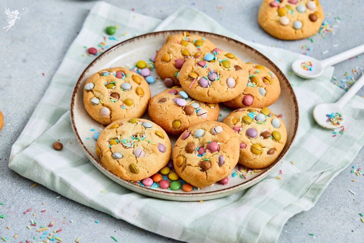 Freshly baked Easter soft cookies with pastel chocolate beans and colorful sprinkles on a rustic plate and checkered linen.