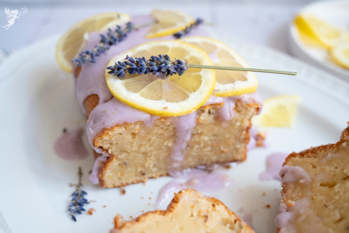A thick slice of Lemon Lavender Pound Cake topped with purple citrus glaze, fresh lemon wheels, and aromatic dried lavender sprigs.