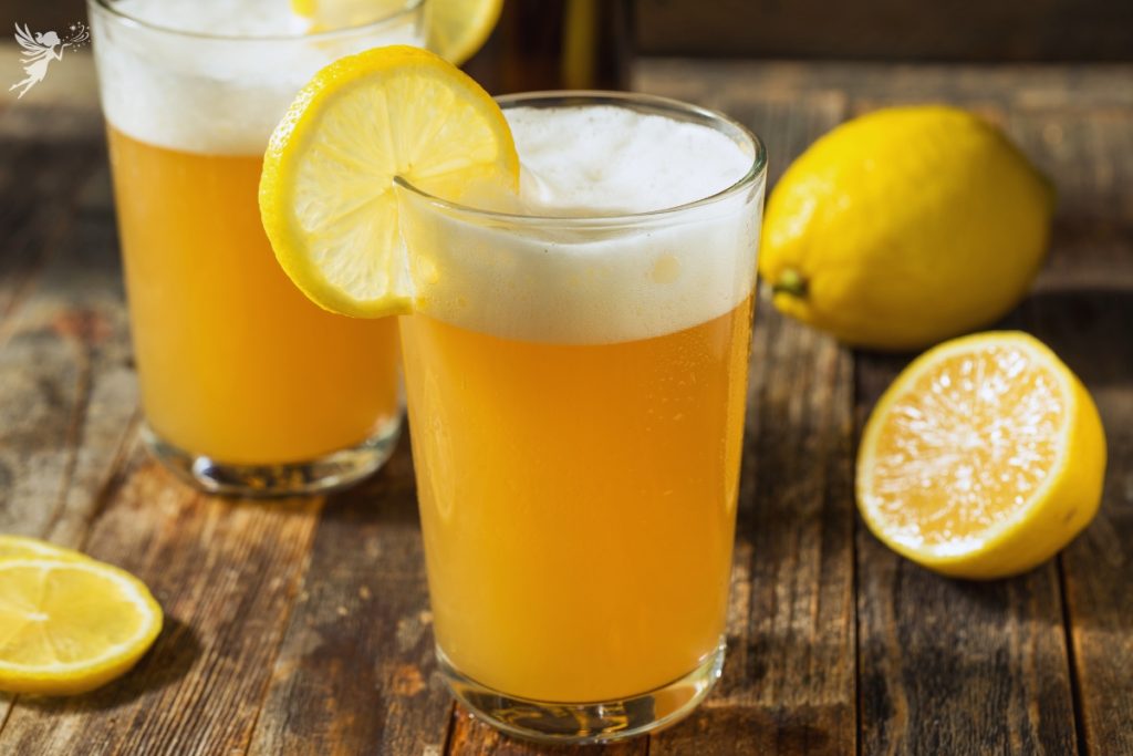 refreshing lemon shandy glasses on a wood surface with chopped lemons