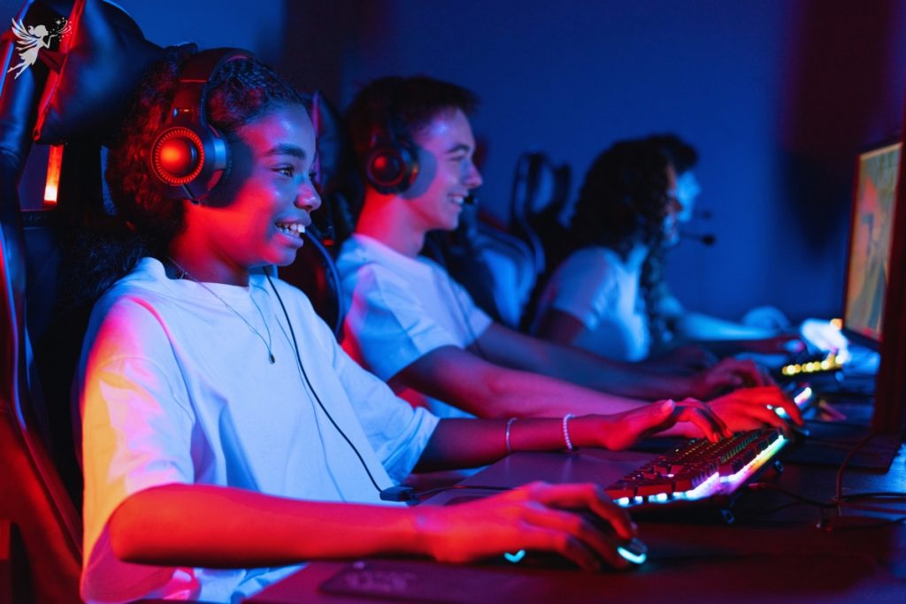 row of teenagers in the dark sitting on computer consoles with headsets laughing and having fun