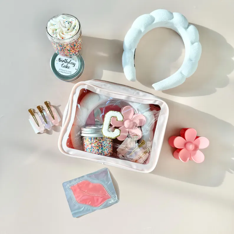 A clear-windowed pink pouch containing a white bubble headband, flower claw clip, and birthday cake candle for sleepover party favors.