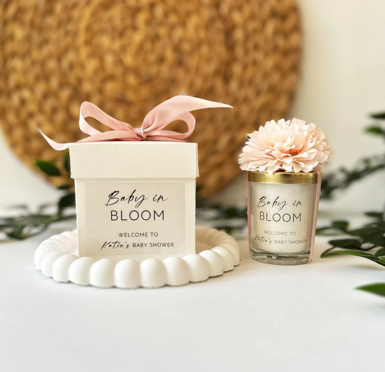 Elegant "Baby in Bloom" personalized candle in a glass vessel topped with a pink flower alongside a matching gift box with pink ribbon, charming baby shower party favors for guests. Etsy