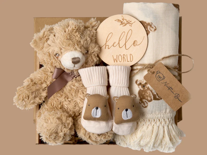 Neutral teddy bear gift set including a plush bear, bear-face socks, muslin blanket, and Hello World wooden disc, a warm and cuddly baby shower gift for newborns.