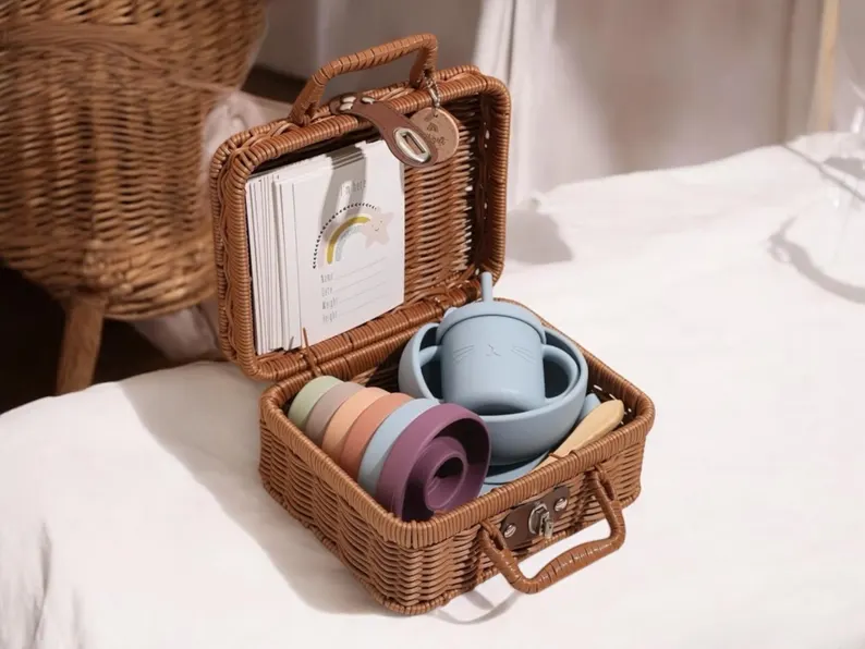 Small rattan suitcase filled with pastel silicone stacking rings, a cat sippy cup, milestone cards, and wooden spoon, an adorable curated baby shower gift hamper.
