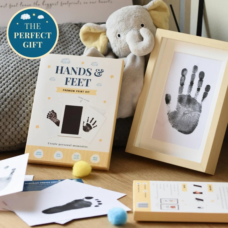 Baby hands and feet premium ink print kit displayed beside a framed handprint and elephant stuffed toy, a thoughtful and memorable baby shower gift for new parents.