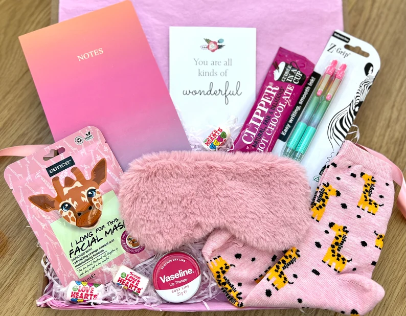 A pink gift box filled with a face mask, fuzzy eye mask, giraffe socks, and treats for sleepover party favors.