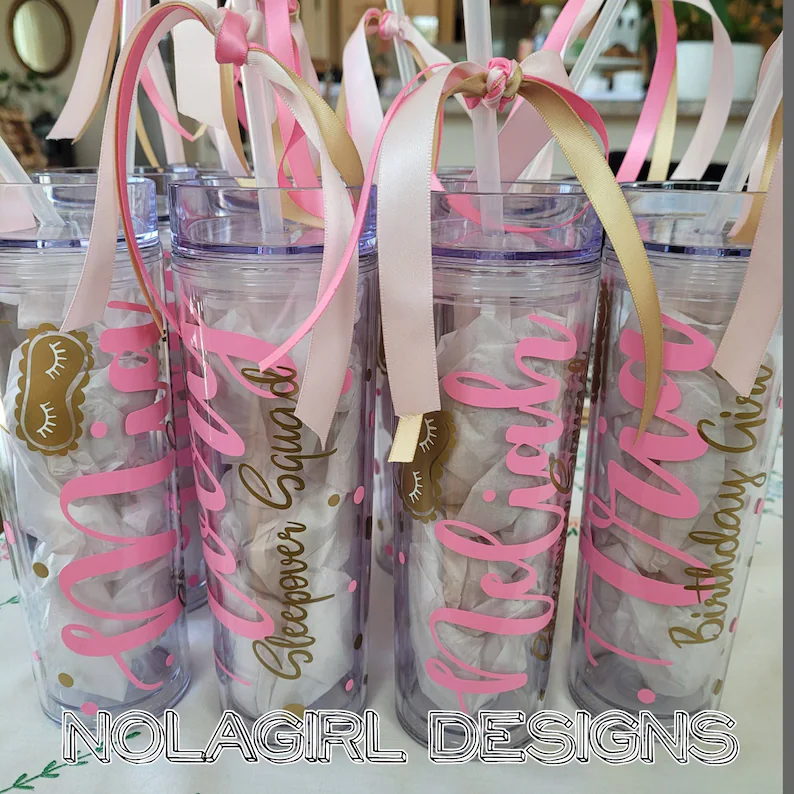 Clear acrylic tumblers with personalized names and decorative ribbons, practical sleepover party favors for girls' birthday slumber party celebrations.