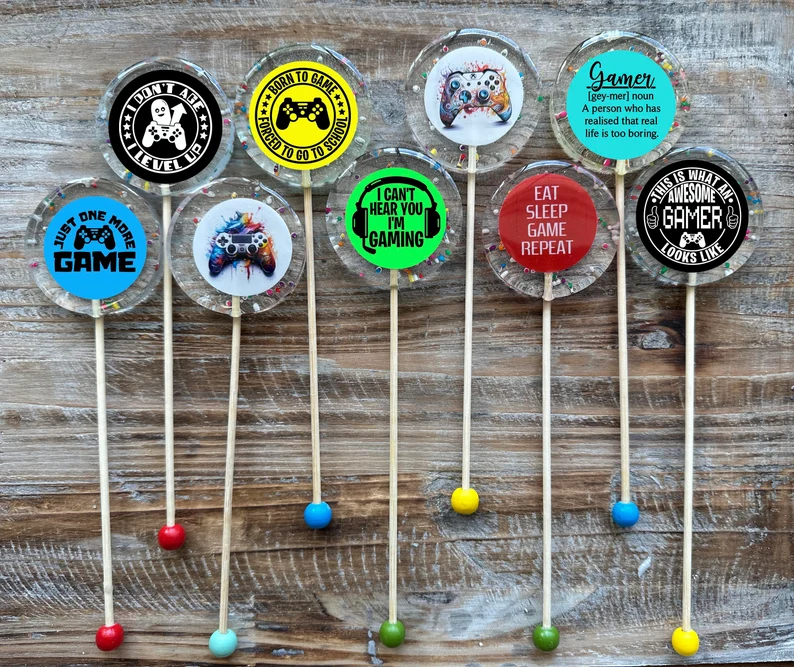 Gamer-themed clear hard candy lollipops with colorful gaming quotes and controller designs, sweet tween teen boy party favors for video game birthday parties.