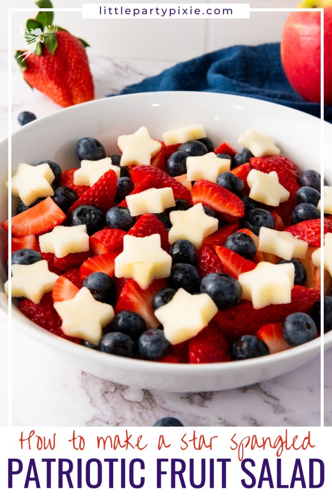 White bowl filled with star spangled fruit salad featuring red strawberries, blue blueberries, and white star-shaped apple pieces with fresh berries.
