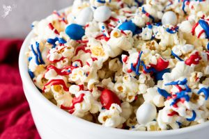 Bowl of red white and blue patriotic popcorn drizzled with red and blue candy melts and topped with M&Ms and sprinkles.