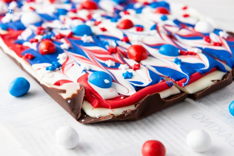 Close-up of Red White & Blue Chocolate Bark slab showing dark chocolate base with white chocolate layer topped with red and blue swirls and candies.