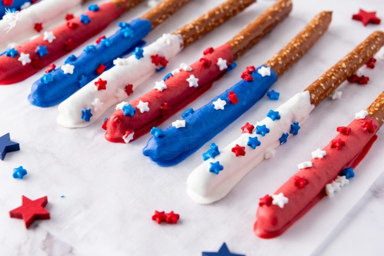 Close-up of patriotic Red White Blue Firecracker Pretzel Rods coated in red, white, and blue chocolate with star sprinkles on white background.