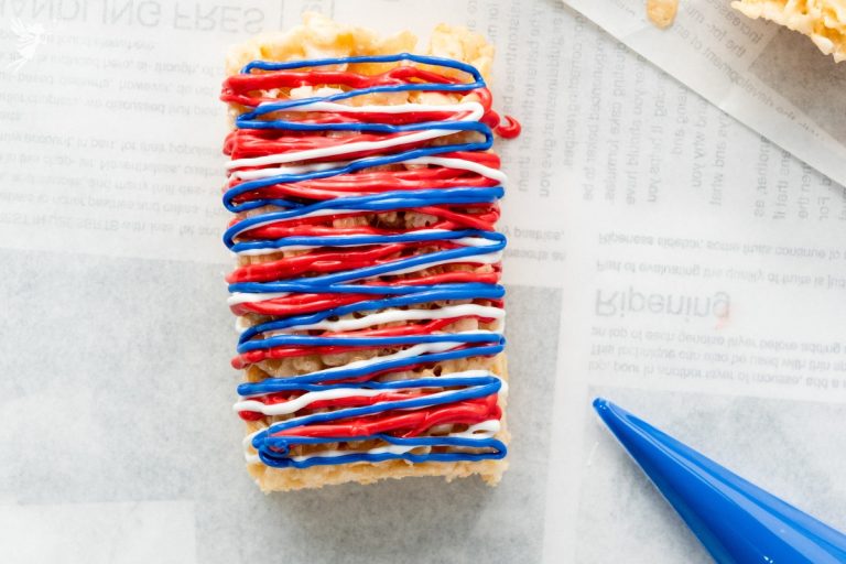 Close-up overhead view of single Patriotic Rice Krispie Treat bar decorated with zigzag red, white, and blue candy drizzle on parchment paper.