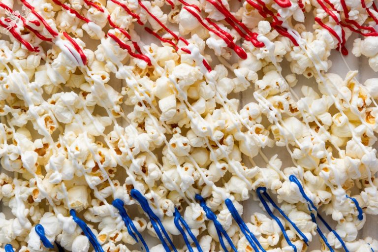 Close-up overhead view of red white and blue patriotic popcorn showing red and blue candy drizzle over fluffy white popcorn.
