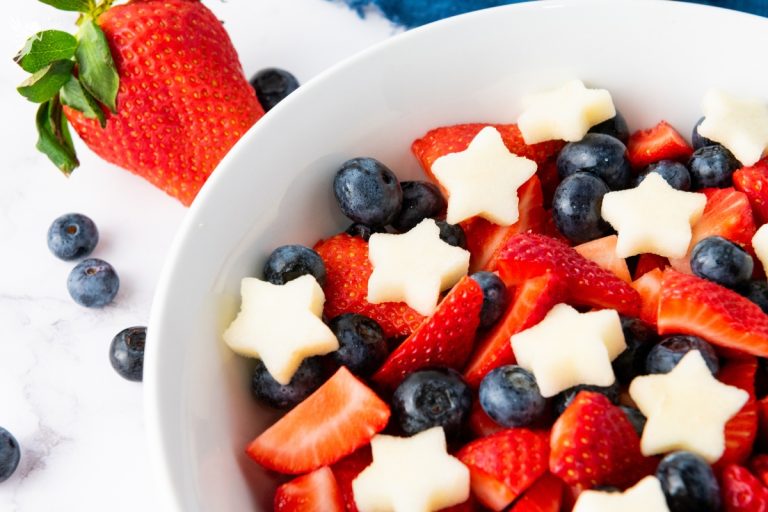 Close-up of star spangled fruit salad showing sliced strawberries, whole blueberries, and star-shaped apple chunks in white bowl.