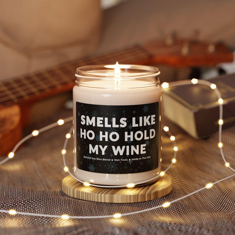 Funny wine-themed candle with "Ho Ho Hold My Wine" label surrounded by fairy lights—perfect unique wine lover gift ideas for Christmas. Etsy