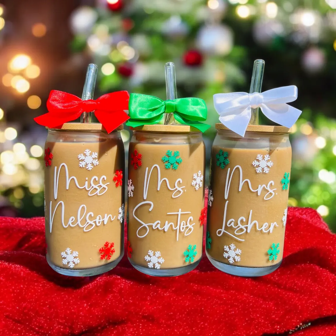 Personalized glass coffee mugs as teacher appreciation gifts decorated with snowflakes, colorful ribbon bows, and teacher names against festive holiday backdrop. Etsy