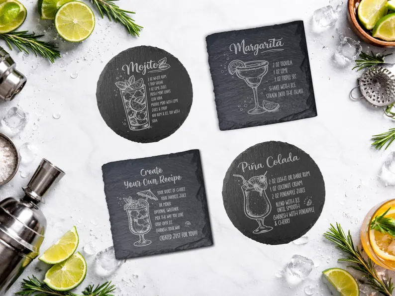 Set of dark slate coasters etched with classic cocktail recipes and drink sketches surrounded by fresh limes and barware—creative gifts for cocktail lovers. Etsy