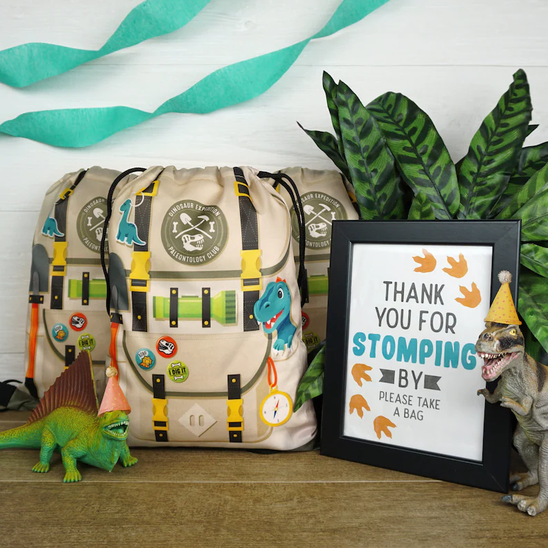 Dinosaur drawstring bag dino party favors styled as explorer backpacks with paleontology patches, colorful straps, and decorative pins beside jungle plants and thank-you sign. Etsy