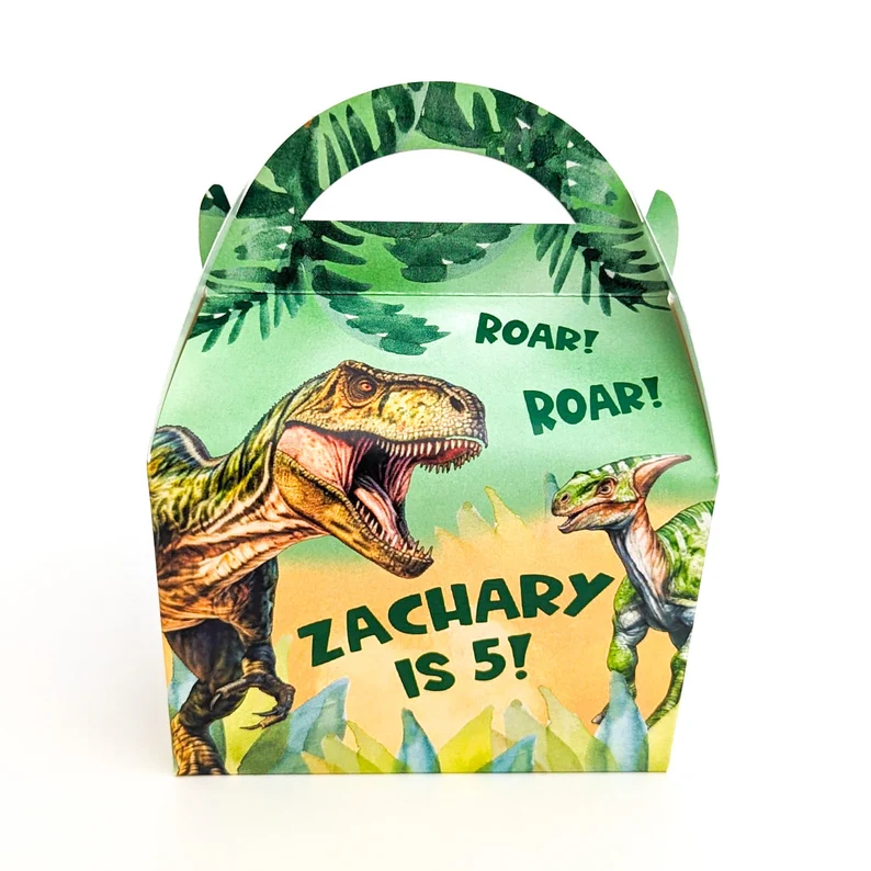 Dinosaur paper party box dino party favors with tropical leaf design, featuring roaring T-Rex illustration and personalized text reading "Zachary is 5" on green jungle background. Etsy
