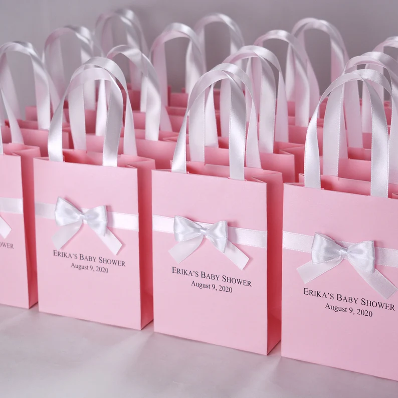 Elegant party bags with ribbon baby shower party favors displayed as pink gift bags with white satin bows, handles, and personalized event text. Etsy