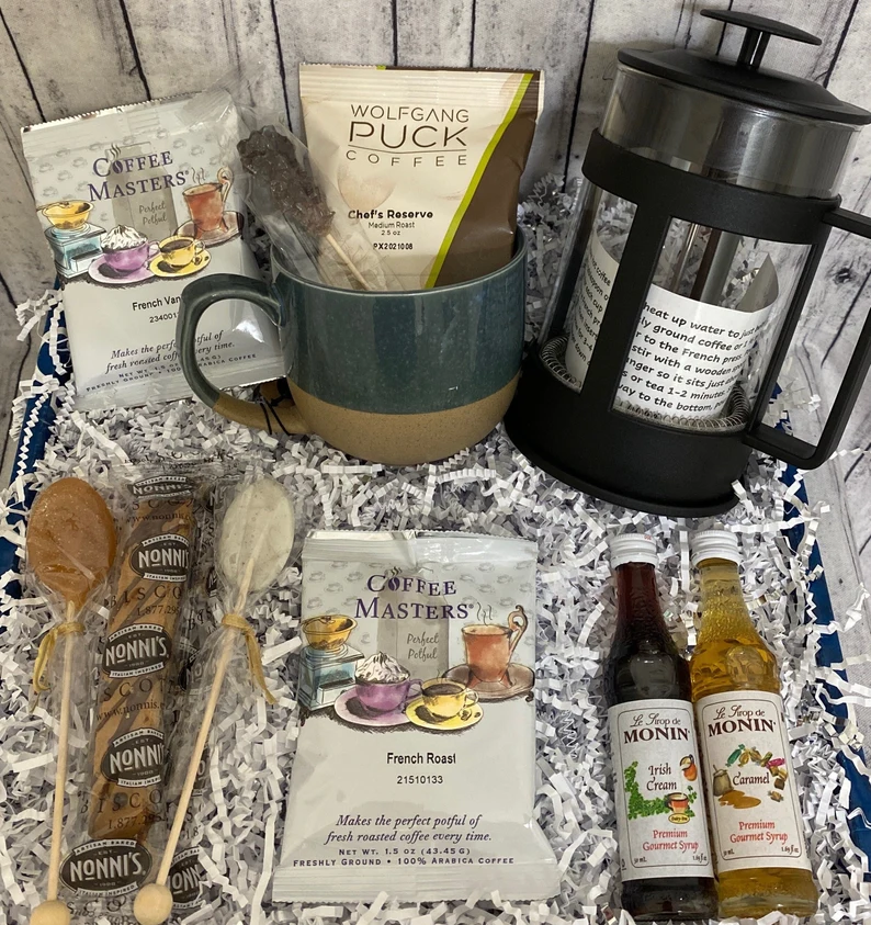 Gourmet coffee gift basket with Wolfgang Puck beans, French press, flavored syrups, and biscotti on white shredded paper—premium coffee lover gift ideas collection. Etsy