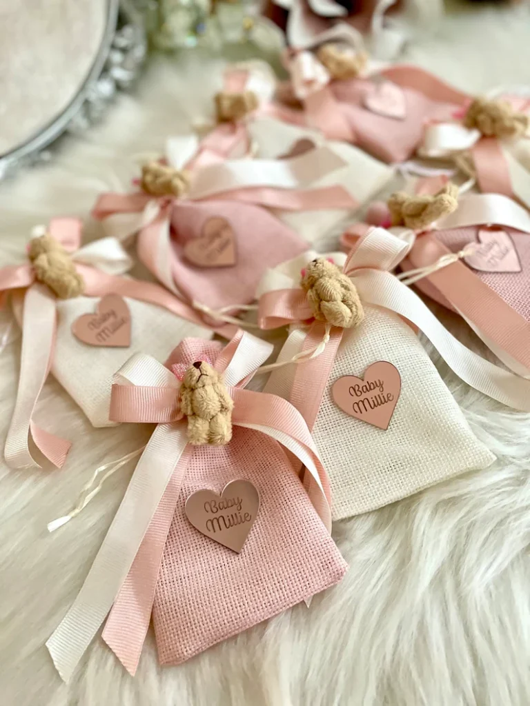 Teddy cloth bags baby shower party favors in pink and cream textured fabric pouches, decorated with small teddy bear charms, ribbons, and personalized heart tags. Etsy