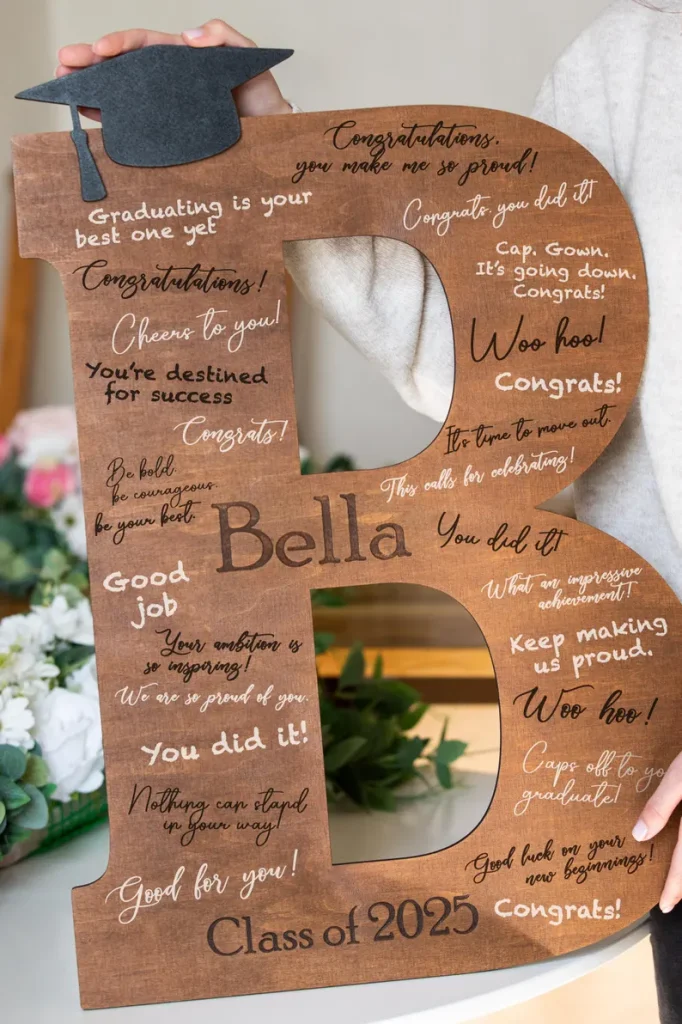 Large wooden letter B personalized for Bella covered in handwritten congratulatory messages and topped with a graduation cap, one of the most memorable graduation gifts. Etsy