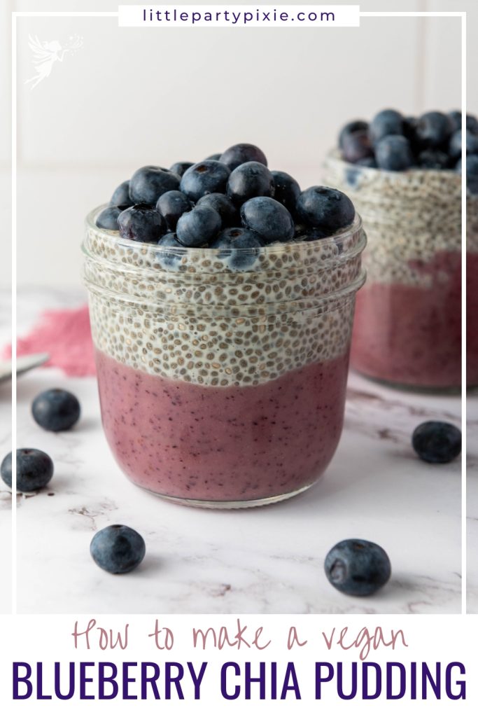 A blueberry chia pudding cup with distinct purple and white layers topped with fresh blueberries surrounded by scattered berries on marble.