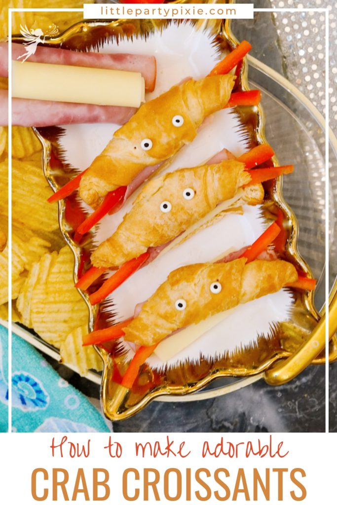 An image showing adorable crab croissants recipe with mini croissants shaped like crabs using string cheese, ham, red pepper strips, and candy eyes on a gold serving tray.