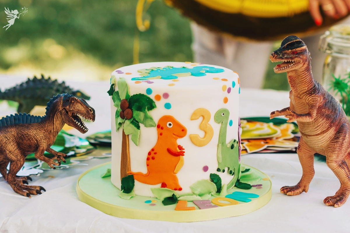 dino party themed cake with cute dinosaurs cut out in fondant and number 3 surrounded by plastic dino decorations