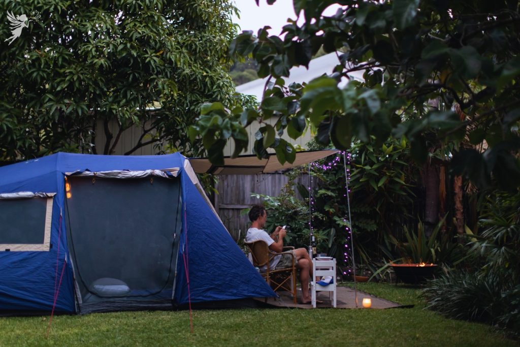 man sitting outside a big blue tent set up in a backyard