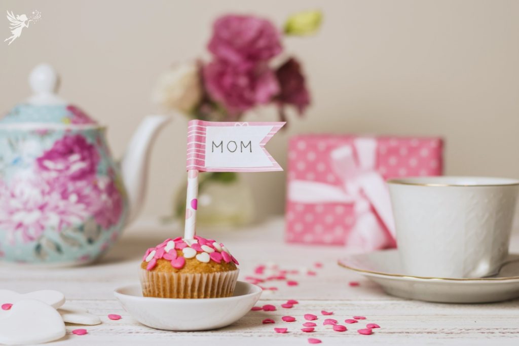 a pink and white vanilla cupcake with a cake topper saying Mom
